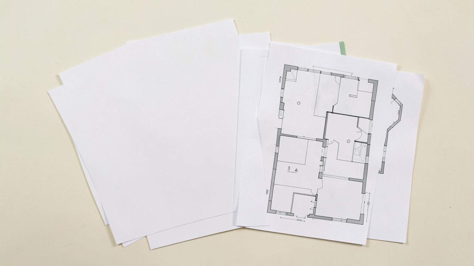 Blank documents, a site plan and a floor plan laid side by side and overlapping on a warm off-white table