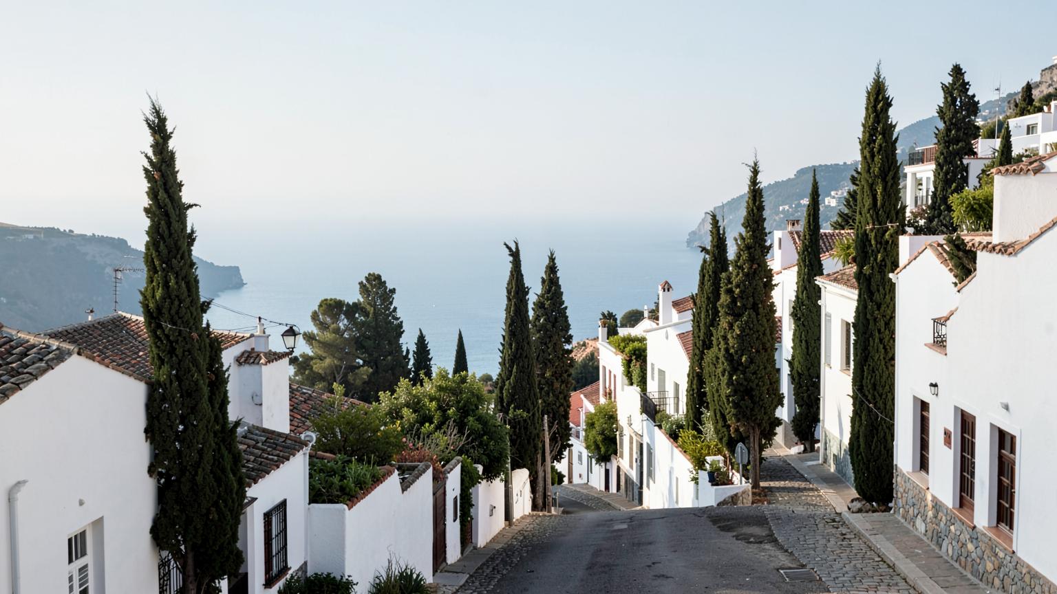 Quiet Andalusian hillside street with white villas and cypress trees overlooking the Mediterranean sea